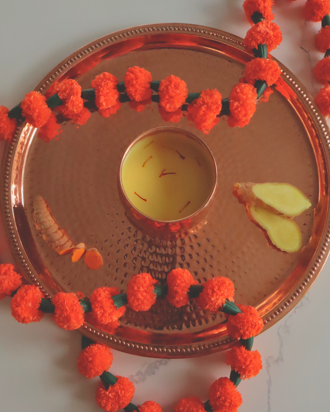 Copper tray with a golden milk Tula fiber latte, marigold flowers, and ginger on a white background